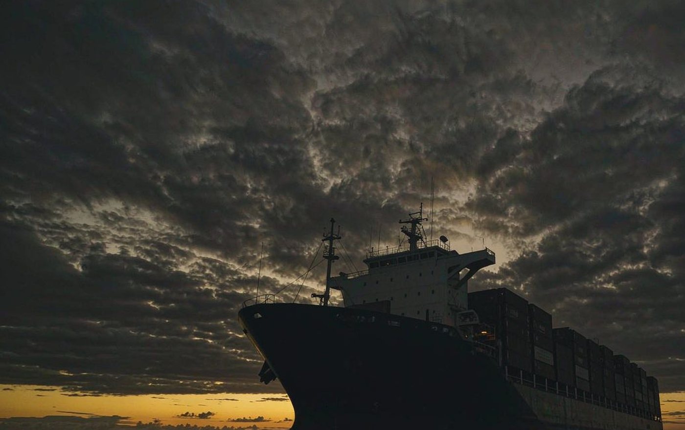 Container ship silhouetted against storm clouds at sea