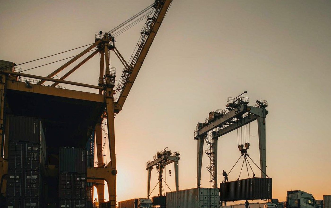 Port gantry cranes lifting a shipping container onto a truck at sunset